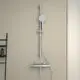 Brausethermostat von Ideal Standard mit verstellbarer Handbrause und Wandmontage, kombiniert mit einem Ablagebereich für Duschutensilien an einer neutralen Wand.